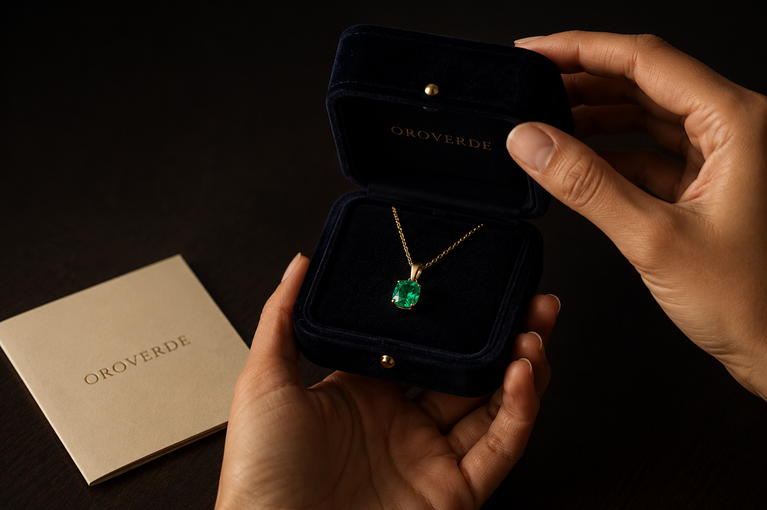 Manos sosteniendo caja OROVERDE abierta con dije de esmeralda colombiana en oro 18k y certificado de marca
